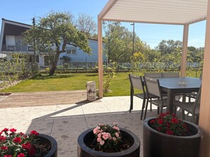 An outdoor patio area with a table and chairs, potted plants, and a view of a residential area.