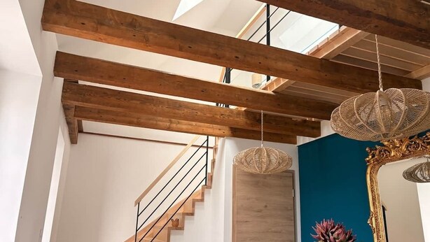 Un intérieur moderne avec des poutres apparentes, un escalier en colimaçon, une porte en bois et un mur d’accent bleu.