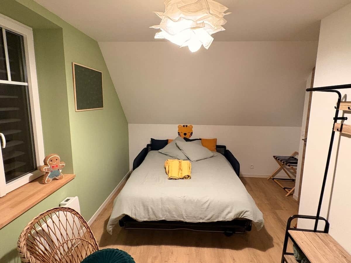 A bedroom with a bed, a window, a teddy bear, and a lamp.