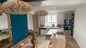 Une cuisine moderne avec un îlot central, une table à manger en bois avec des chaises, et un grand miroir.