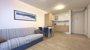 Ein modernes Wohnzimmer mit einem gestreiften Sofa, einem Esstisch mit Stühlen, einer Küchenzeile inklusive Schränke und Mikrowelle sowie einem gerahmten Bild an der Wand.
