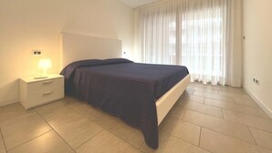 Ein Schlafzimmer mit einem Bett, einem Nachttisch, einer Lampe und einem Fenster mit Vorhängen.