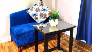 A corner room with a blue sofa, a floral pillow, a small table with a plant, and a blue curtain. - Horus Guest House Pyramids  (Giza)