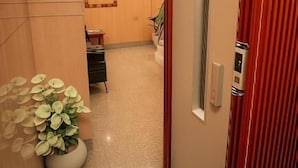 A hallway with a red door, a potted plant, a chandelier, and a small table with a chair. - Horus Guest House Pyramids  (Giza)