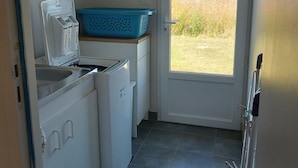 Eine kleine Küche mit Waschmaschine, einem Spülbecken und einem blauen Wäschekorb.