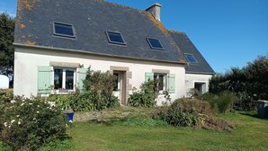 Ein zweistöckiges Haus mit geneigtem Dach, einem Schornstein und einem kleinen Garten mit verschiedenen Pflanzen und Blumen.