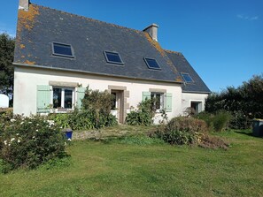 A two-story house with a sloped roof, a chimney, and a small garden with various plants and flowers. - Ti Mammig. (Kerlouan)