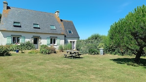 Ein Haus mit geneigtem Dach, einer Veranda und einem Picknicktisch im Garten.