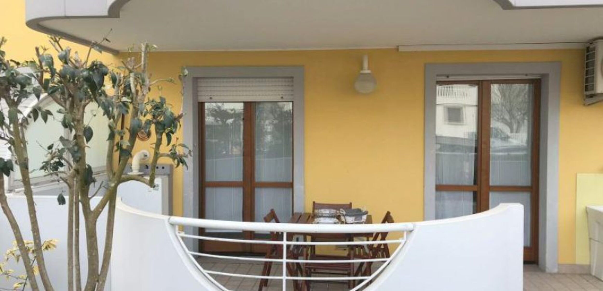 A balcony with a table and chairs, a small plant, and a window with a blind.