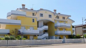 A multi-story building with a yellow facade, balconies, and a curved entrance. - Holiday Home in Grado Close to the Beach (Grado)