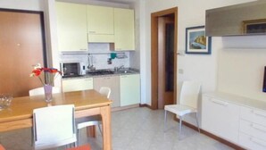 A compact living space with a kitchenette, a dining area, and a TV mounted on the wall. - Holiday Home in Grado Close to the Beach (Grado)