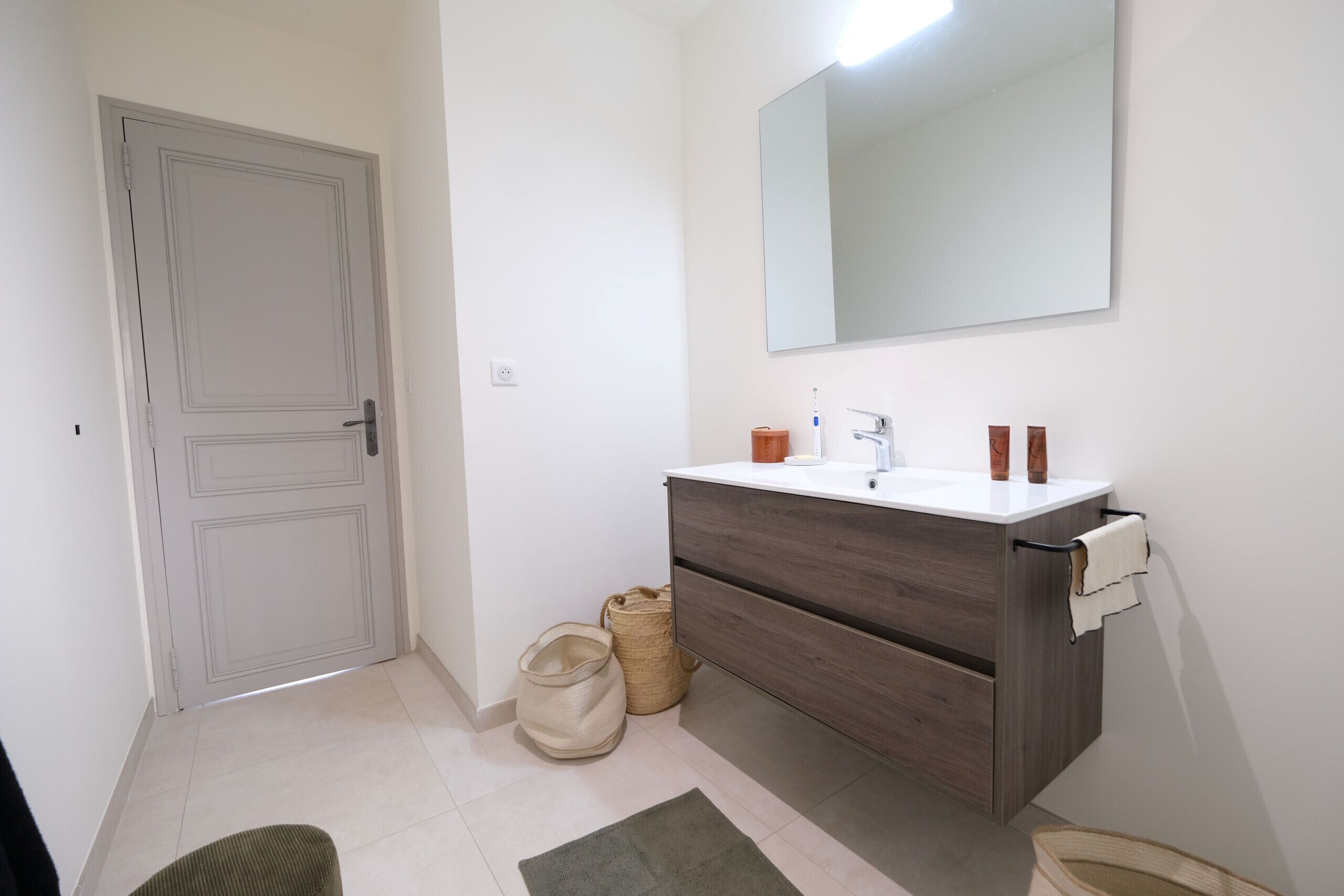 A bathroom with a white door, a mirror above the sink, and a towel rack.