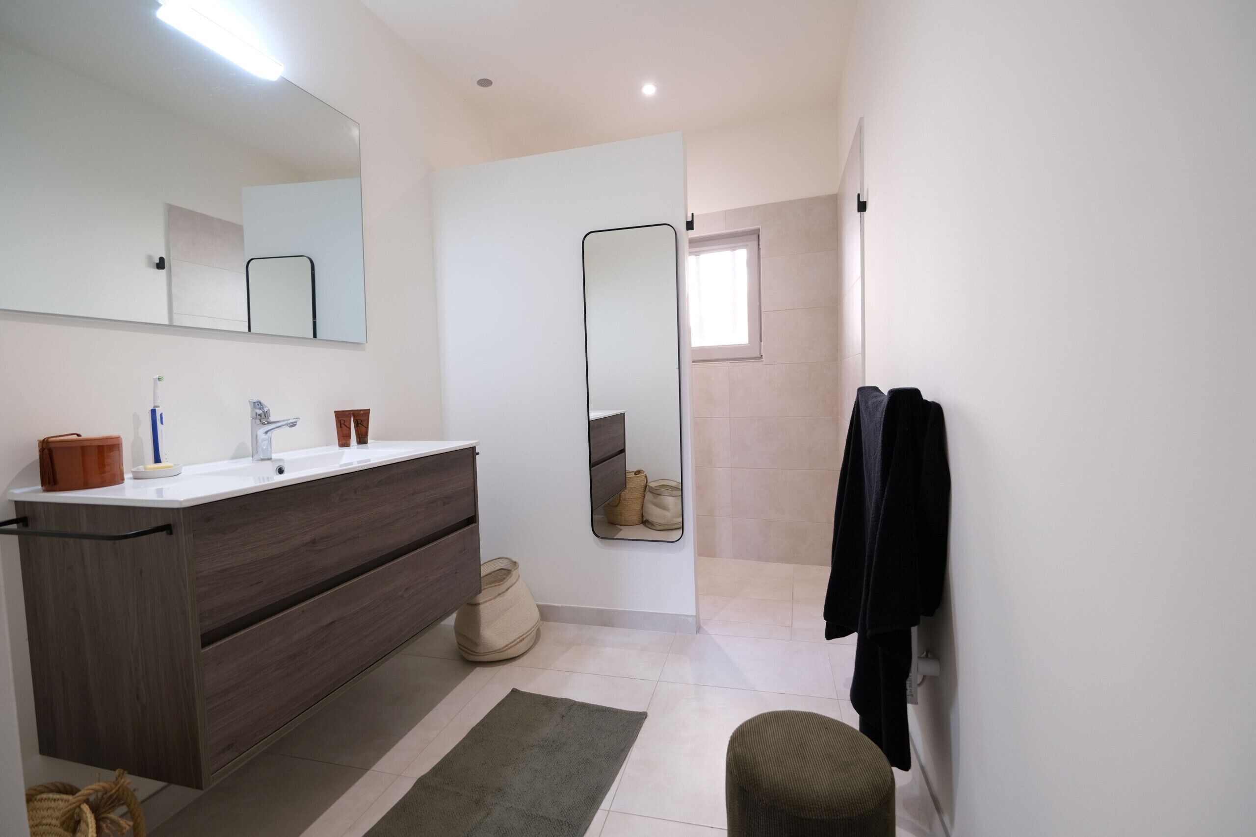 A modern bathroom with a large mirror, a wooden vanity, a towel rack, and a shower area.