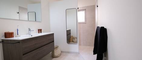 A modern bathroom with a large mirror, a wooden vanity, a towel rack, and a shower area.