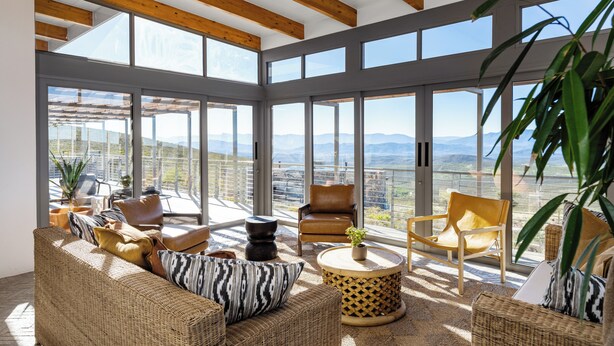 A spacious balcony with wicker furniture, large windows, and a view of the mountains. - Goats Window Luxury Safari Lodge Prestige Collection  (Bonnievale)