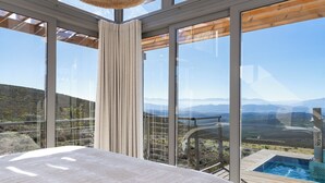 A bedroom with a large window overlooking a mountainous landscape, a wooden deck, and a hot tub. - Goats Window Luxury Safari Lodge Prestige Collection  (Bonnievale)