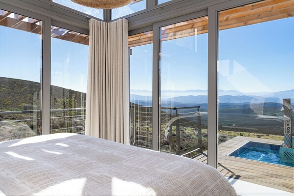 Une chambre avec une grande fenêtre donnant sur un paysage montagneux, une terrasse en bois et un jacuzzi.
