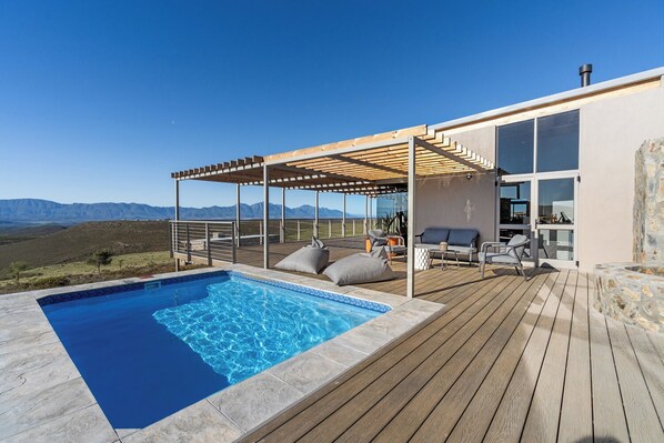 A modern outdoor pool area with a wooden deck, seating, and a view of the mountains. - Goats Window Luxury Safari Lodge Prestige Collection  (Bonnievale)