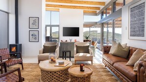 A spacious living room with a fireplace, comfortable seating, and large windows offering a view of the outdoors. - Goats Window Luxury Safari Lodge Prestige Collection  (Bonnievale)