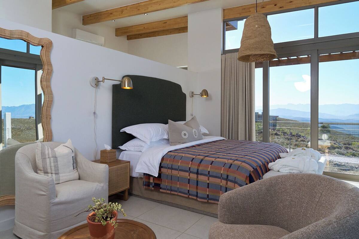 A bedroom with a large bed, a chair, a bedside table, and a view of the mountains.