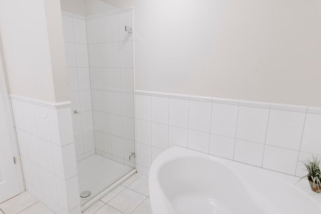 A bathroom with a shower, a bathtub, and white tiled walls.