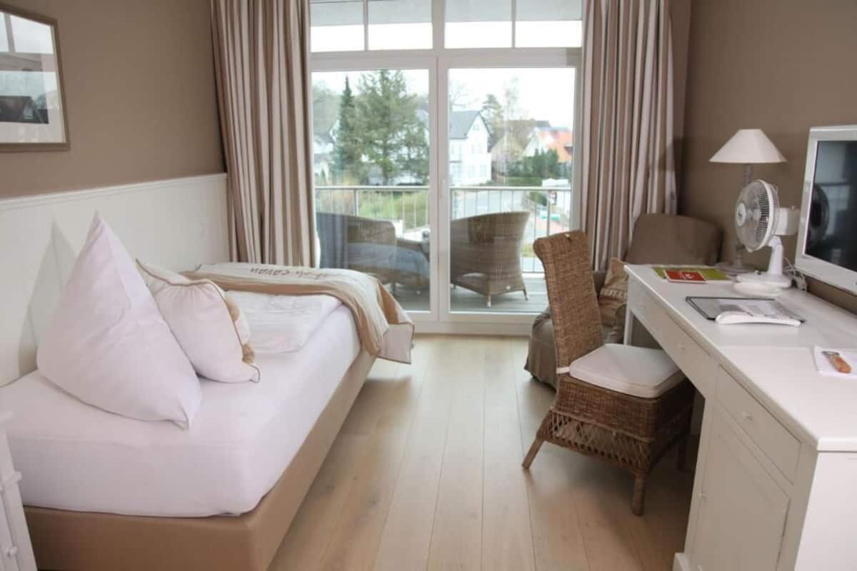 Ein Hotelzimmer mit Bett, Schreibtisch mit Computer, Stuhl und Blick ins Freie.