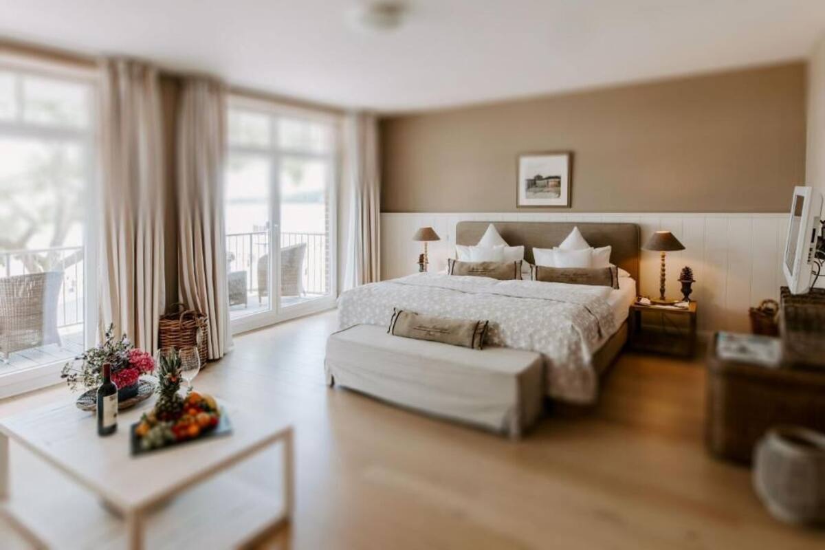 Ein Schlafzimmer mit einem Bett, Nachttischen, Vorhängen an einem Fenster und Blick ins Freie.