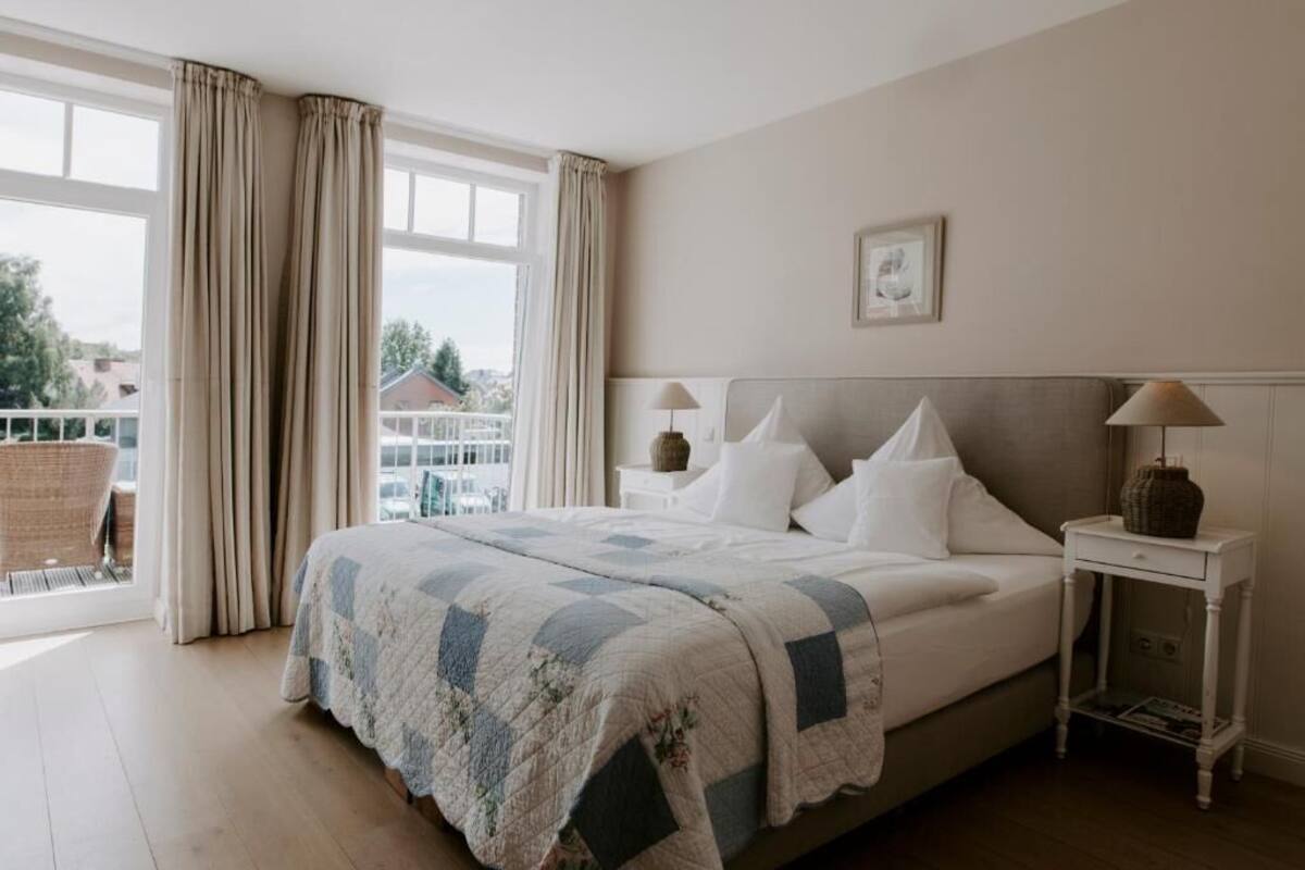 Ein Schlafzimmer mit einem großen Bett, einem Nachttisch, einer Lampe und Blick ins Freie.
