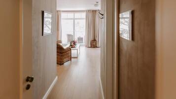Ein Flur, der zu einem Zimmer mit Korbsessel, einem kleinen Tisch mit Blumen und einem fenster mit Vorhängen führt.