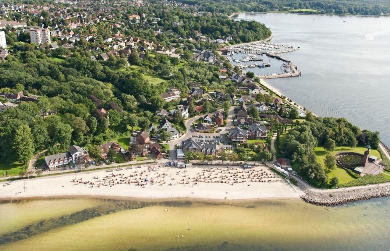 Vue aérienne d’une ville côtière avec un port de plaisance, des zones résidentielles et une plage de sable.
