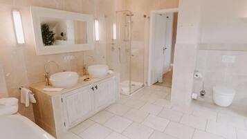 Une salle de bain moderne avec deux lavabos, une baignoire, une douche à parois de verre et des toilettes.