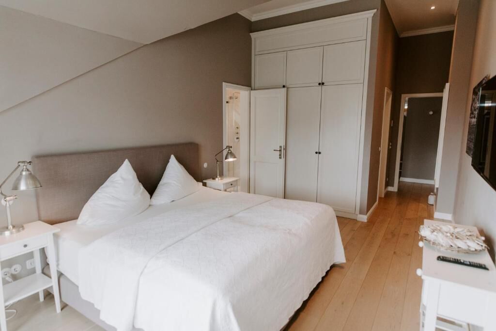A bedroom with a bed, white nightstands, a wardrobe, and a desk with a lamp.