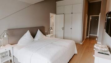 A bedroom with a bed, white nightstands, a wardrobe, and a desk with a lamp.