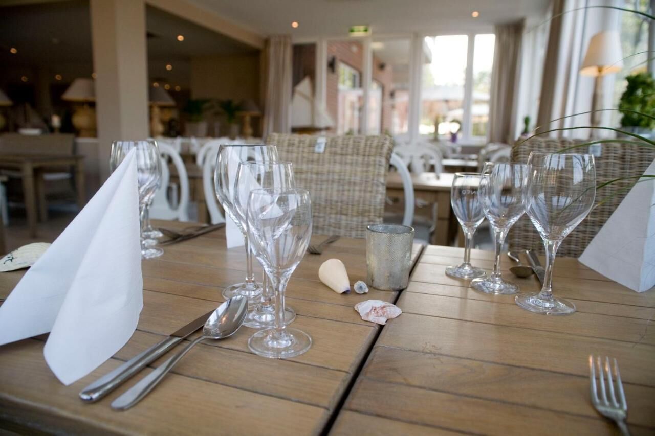Une table à manger dressée avec des verres à vin, des couverts et un menu.