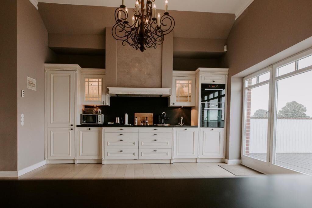 A modern kitchen with white cabinetry, a central island, a built-in oven, and a large window providing natural light.
