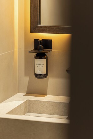 Une bouteille de gel douche WabSabi Suites est accrochée à un mur, au-dessus de laquelle se trouve un cadre en bois.