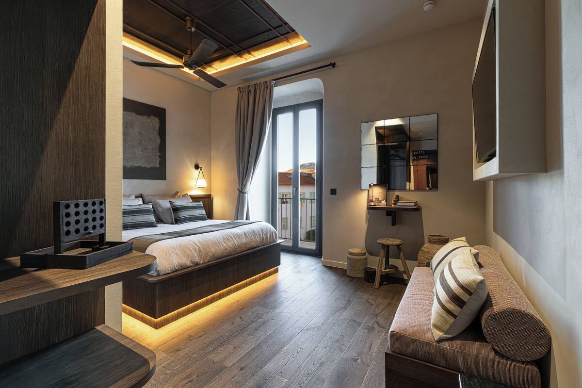 A modern bedroom with a bed, a sofa, a desk, and a large window.
