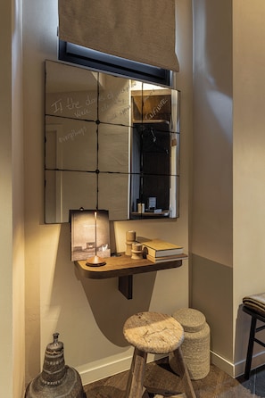 Un coin avec un miroir, une petite étagère avec des livres et une bougie, et un tabouret.