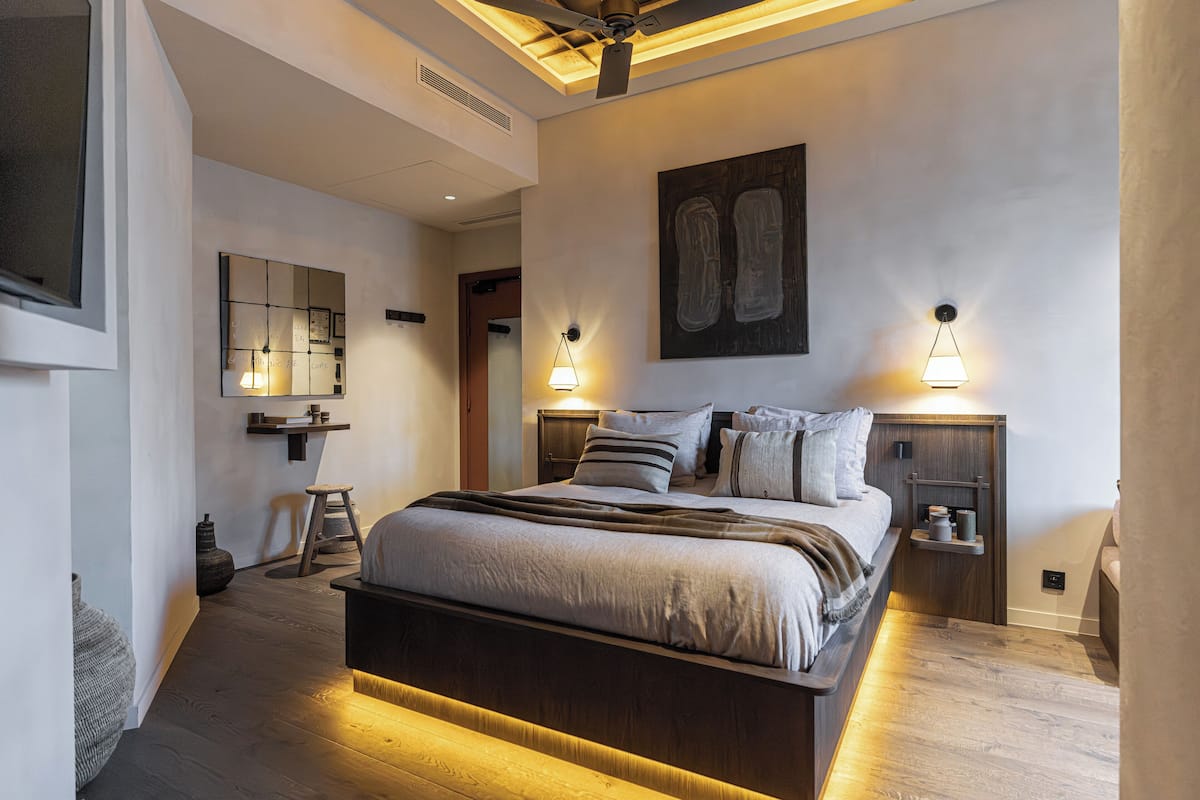 A modern bedroom with a large bed, bedside tables, a ceiling fan, and wall-mounted lighting.