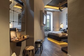 A modern bedroom with a wooden floor, a bed with a headboard, a bedside table with a lamp, and a window with curtains. - Wabi-Sabi Hôtel Lorrain (Nice)