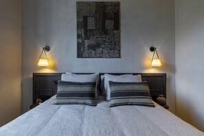 Un lit bien fait, avec deux oreillers, une œuvre d’art abstraite accrochée au mur et deux appliques murales de chaque côté.