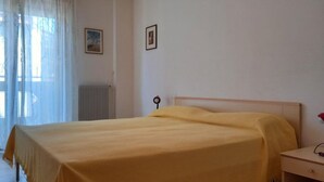 A bedroom with a bed, a nightstand, a radiator, and a window with sheer curtains. - Family Friendly Vacation Apartment With a Balcony (Grado)