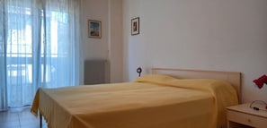 A bedroom with a bed, a nightstand, a radiator, and a window with sheer curtains. - Family Friendly Vacation Apartment With a Balcony (Grado)