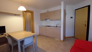A compact room with a kitchenette, a dining area with a table and chairs, a television, and a red couch. - Family Friendly Vacation Apartment With a Balcony (Grado)