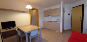 A compact room with a kitchenette, a dining area with a table and chairs, a television, and a red couch. - Family Friendly Vacation Apartment With a Balcony (Grado)