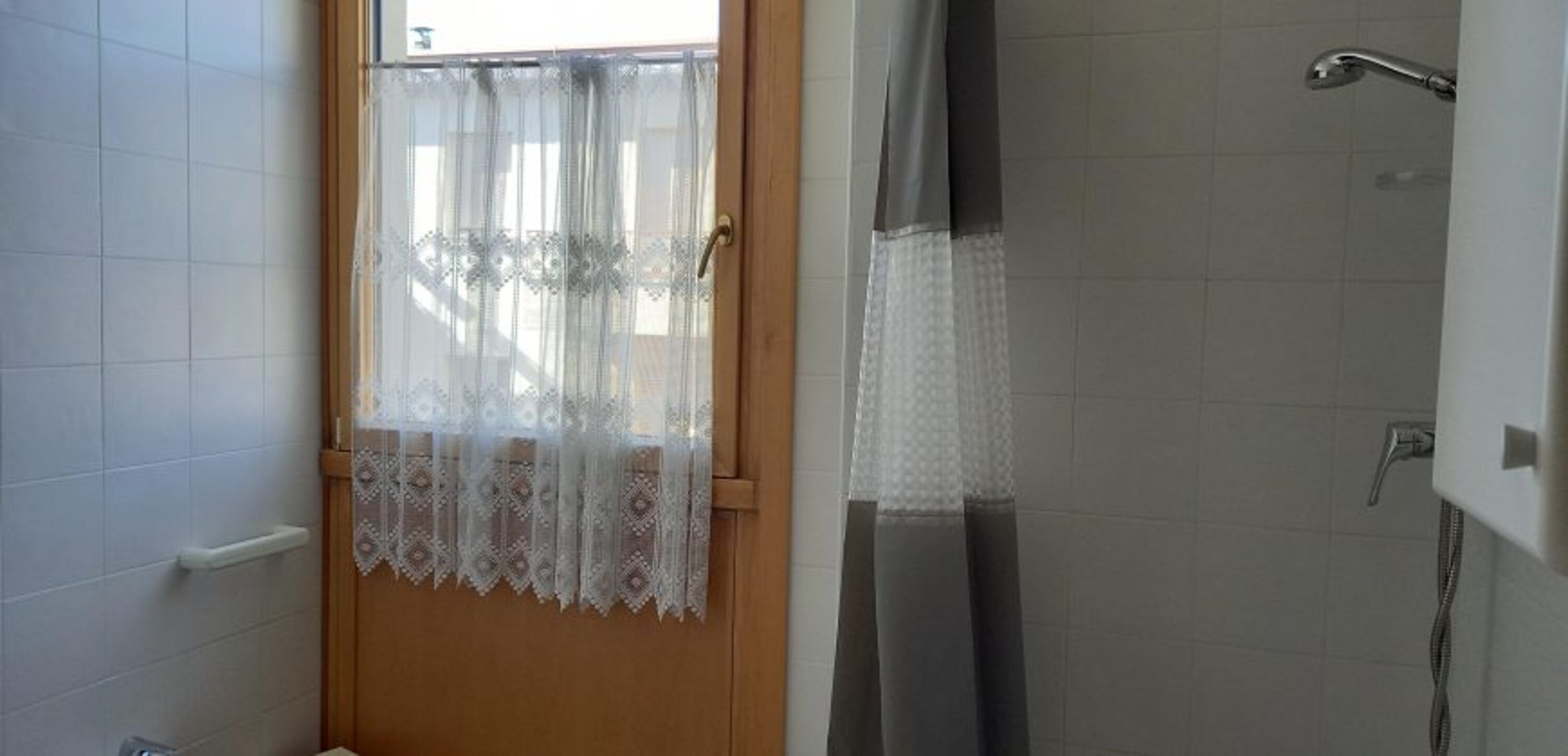 A bathroom with a shower, a toilet, and a window with a lace curtain.