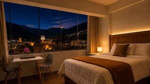 Camera d'albergo con una grande finestra, un letto, una scrivania con una sedia e un comodino.