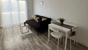 Een moderne woonkamer met een zwarte bank, een kleine witte tafel en een witte eettafel met stoelen.