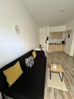 A modern living room with a black sofa, a small table, and a kitchen in the background. - La belle planque- 10 minutos de la Playa- PUNTA CANA (Punta Cana)