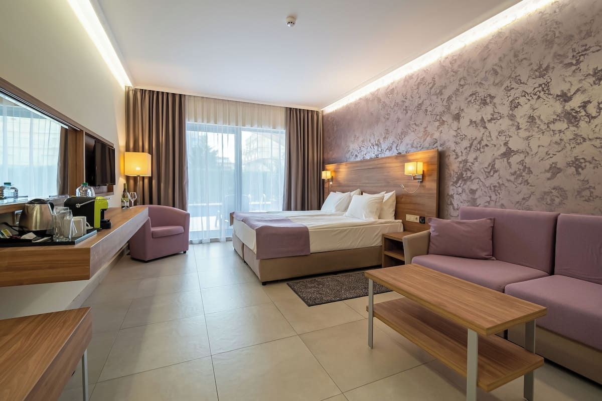 A hotel room with a bed, a sofa, a desk, a TV, and a window with curtains.